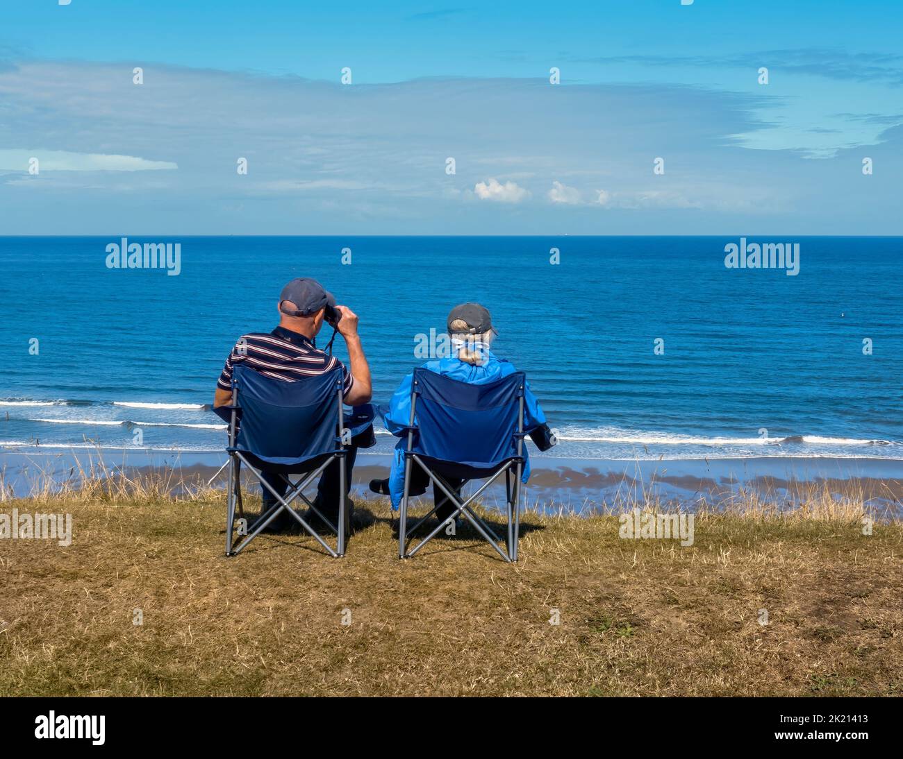 Two people, sitting on collapsible chairs, by the Yorkshire Coast. Stock Photo