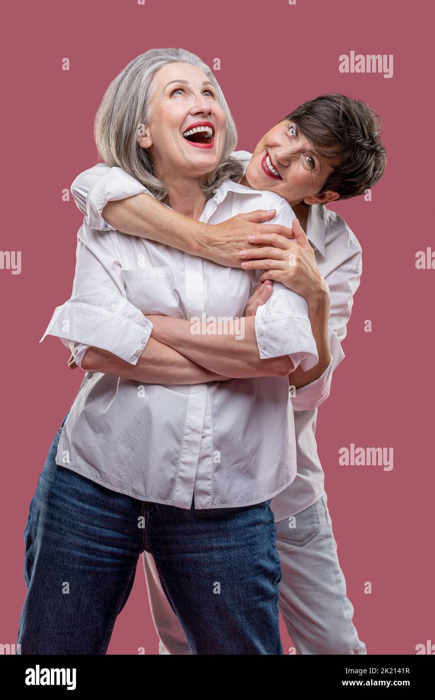 Two cute mature women standing together and hugging Stock Photo