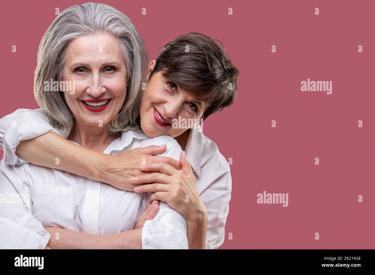 Two cute mature women standing together and hugging Stock Photo