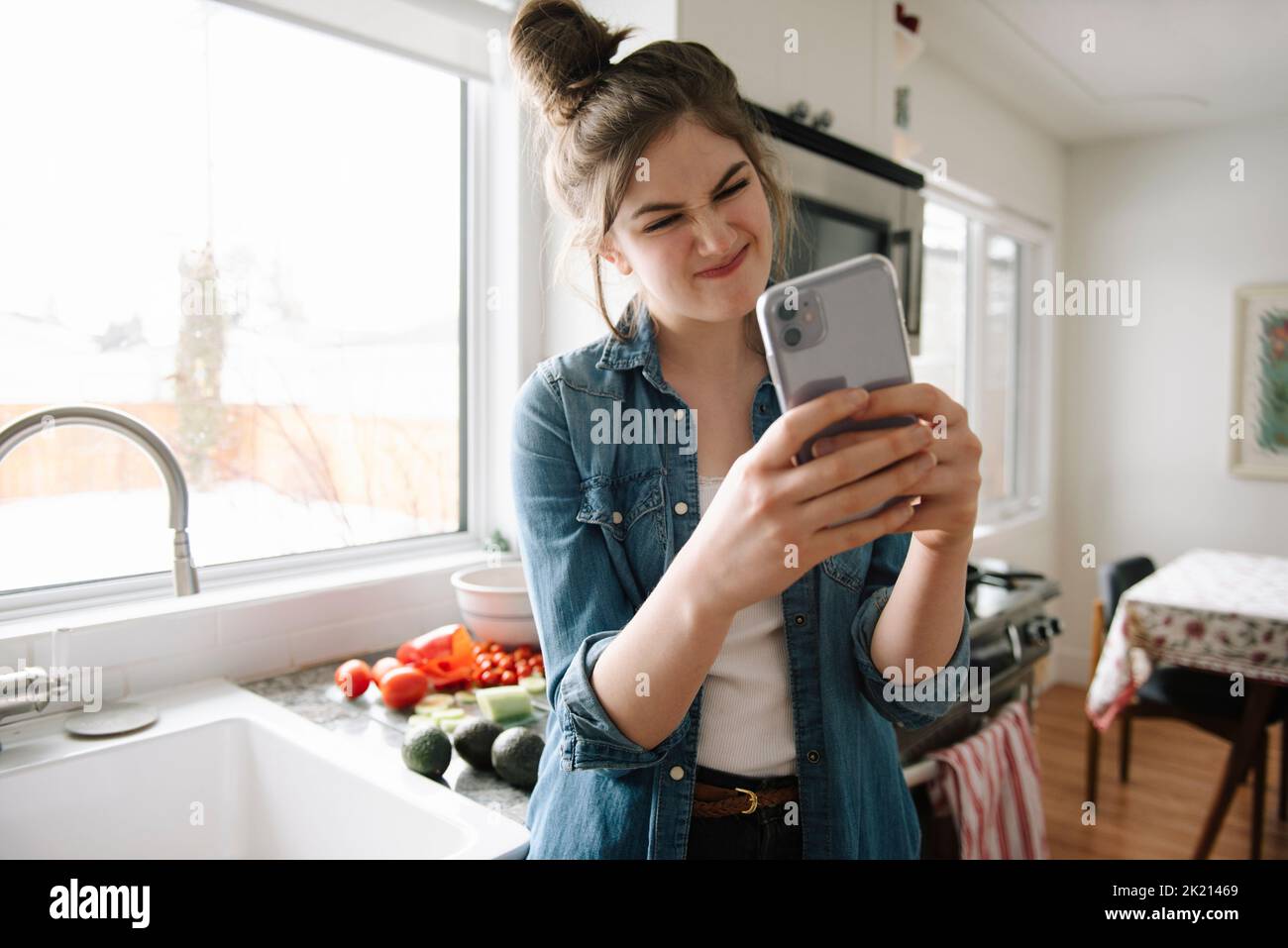 Playful teenage girl making a face and taking selfie in kitchen Stock Photo
