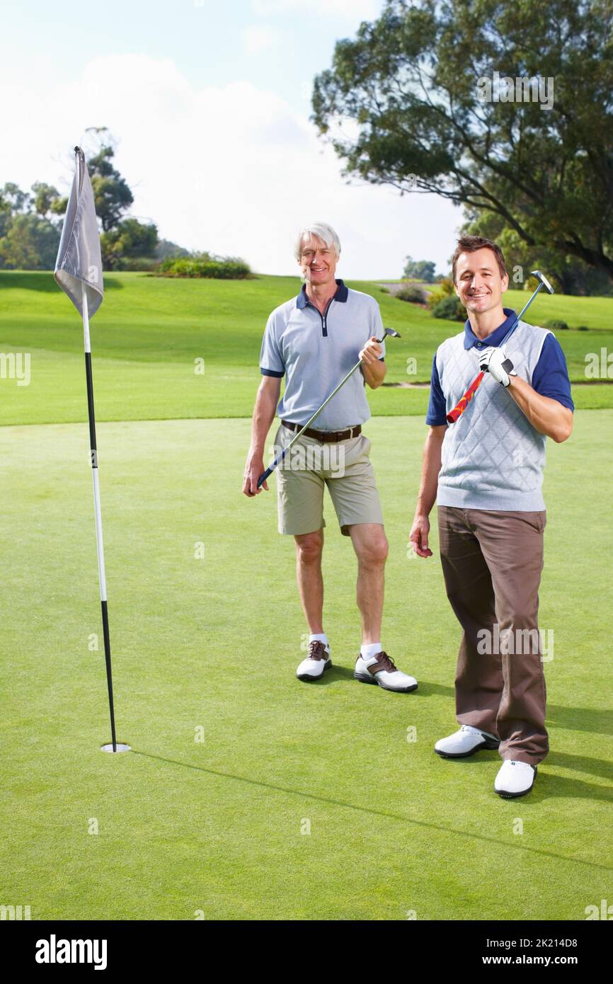 Father and son golfing. Full length of father and son standing on the putting green with golf clubs and smiling. Stock Photo