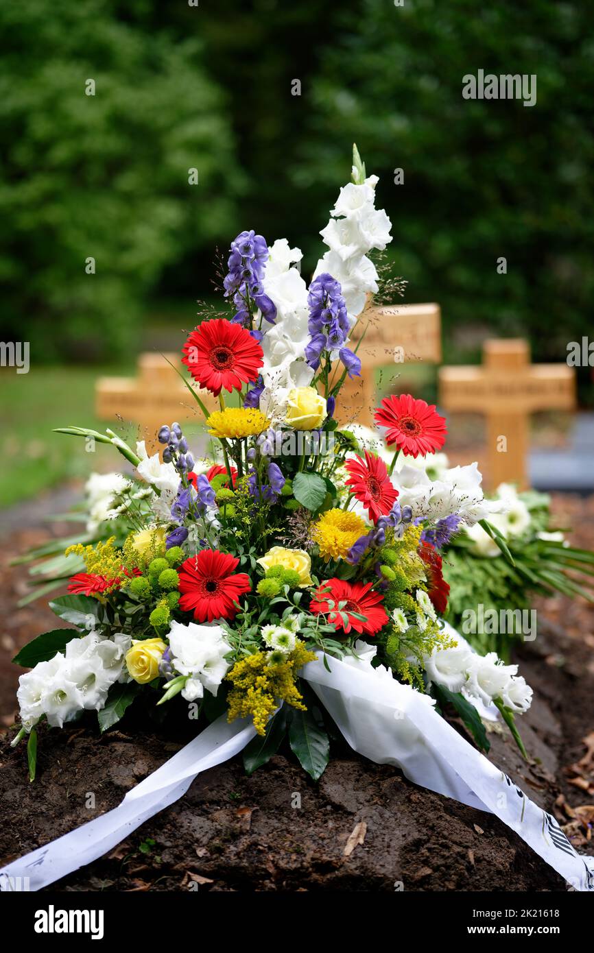 colorful flowers as grave arrangement after a funeral in front of wooden crosses in blurred background Stock Photo