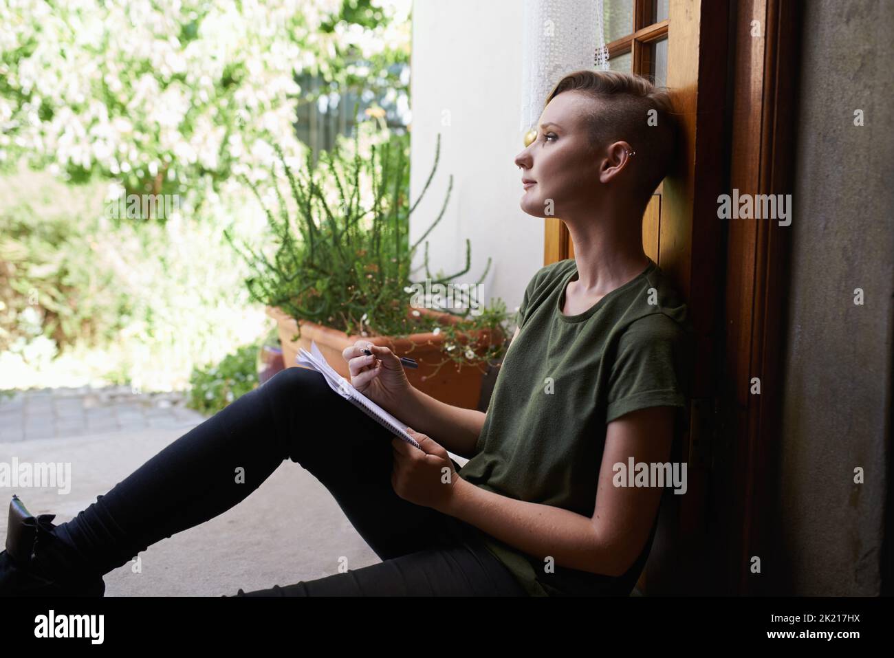 Letting her mind wander. an attractive young woman sitting outside on the porch writing in a notepad. Stock Photo