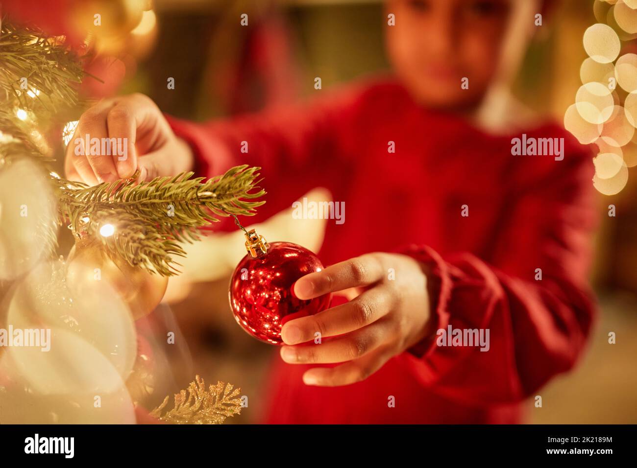 Close up of little girl hanging ornaments on Christmas tree with twinkling lights, copy space Stock Photo