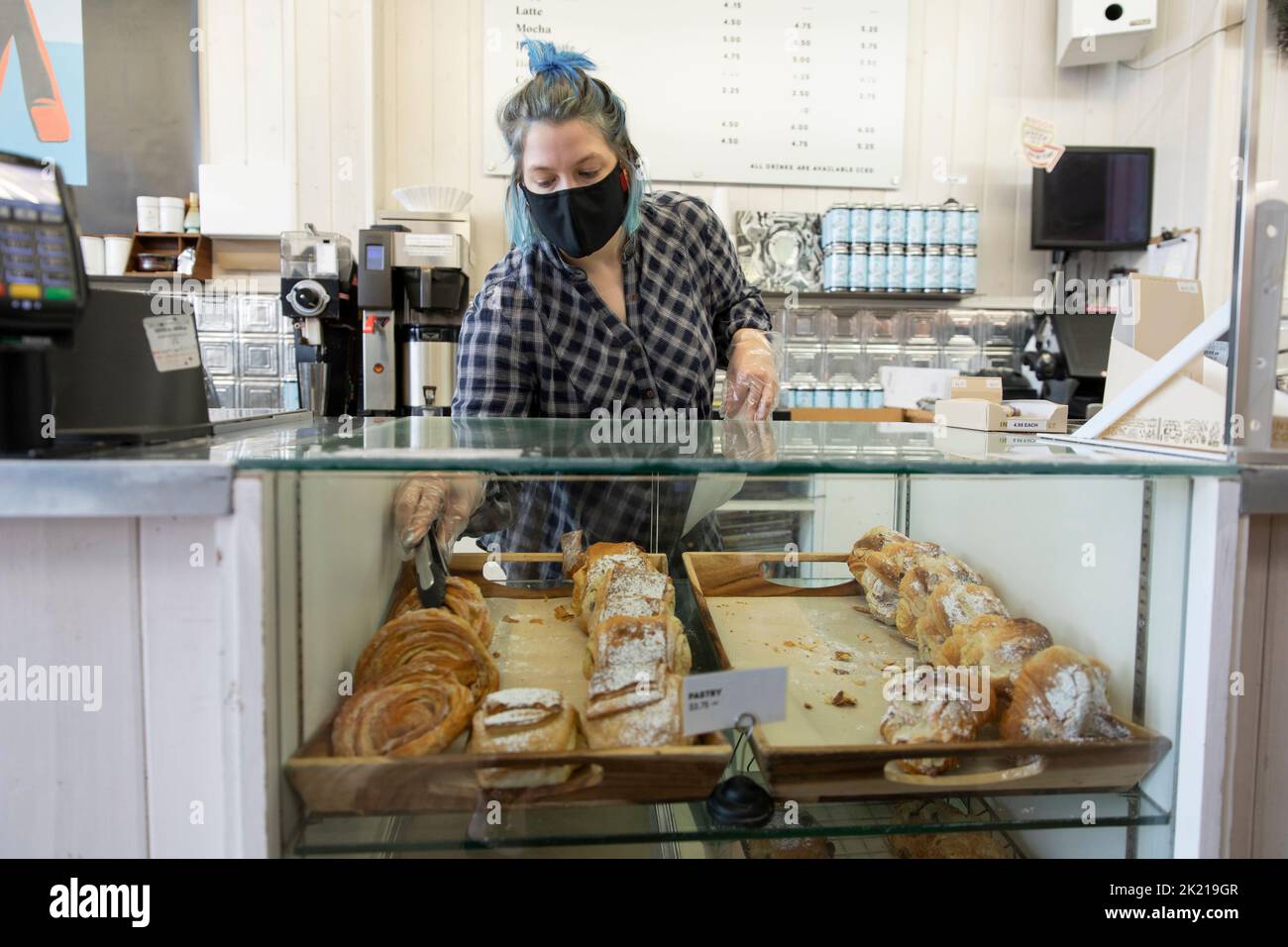 Female worker with blue hair in face mask serving pastries in cafe Stock Photo