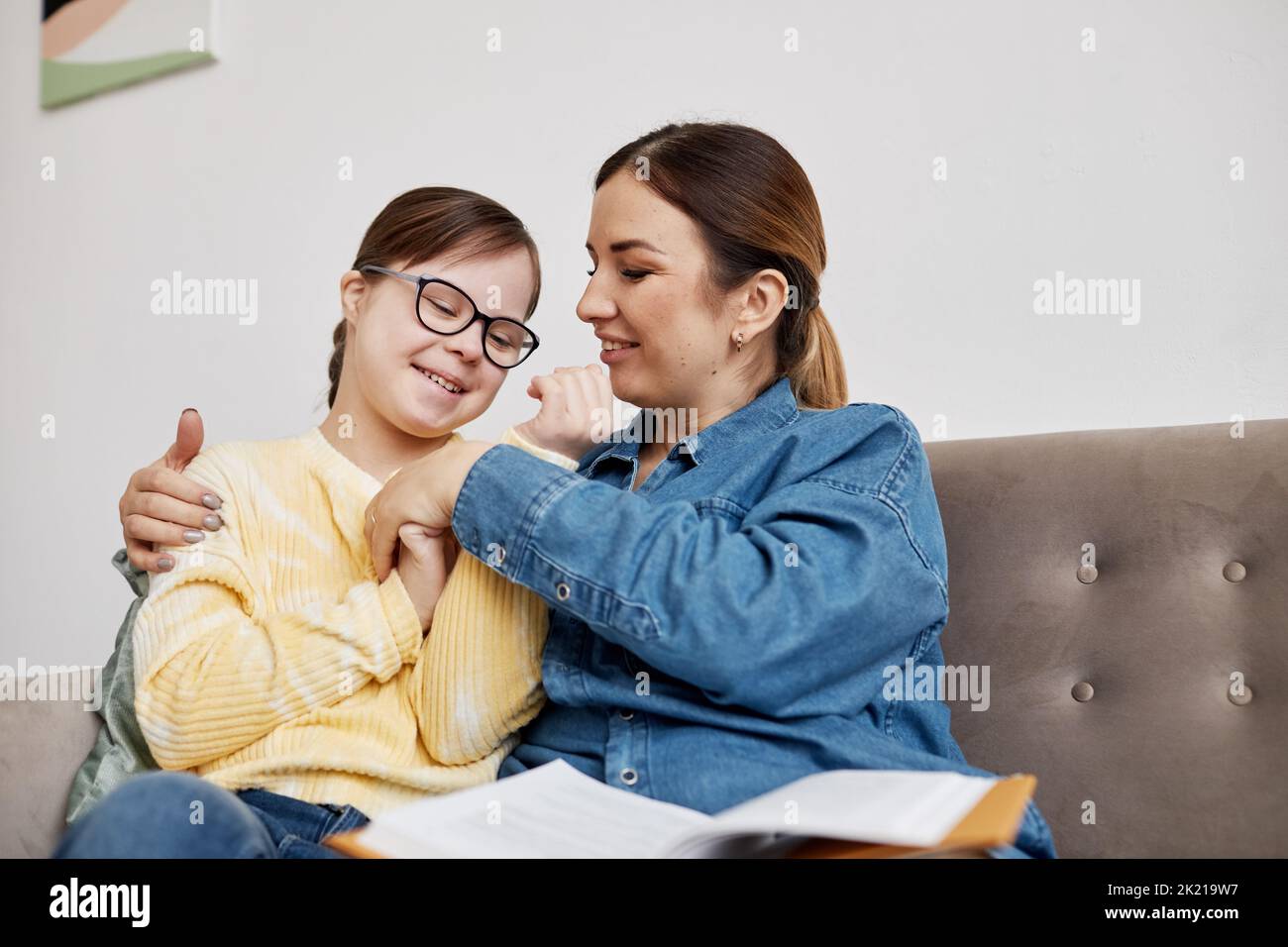 Portrait of happy teenage girl with Down syndrome cuddling with mother while sitting on couch at home Stock Photo