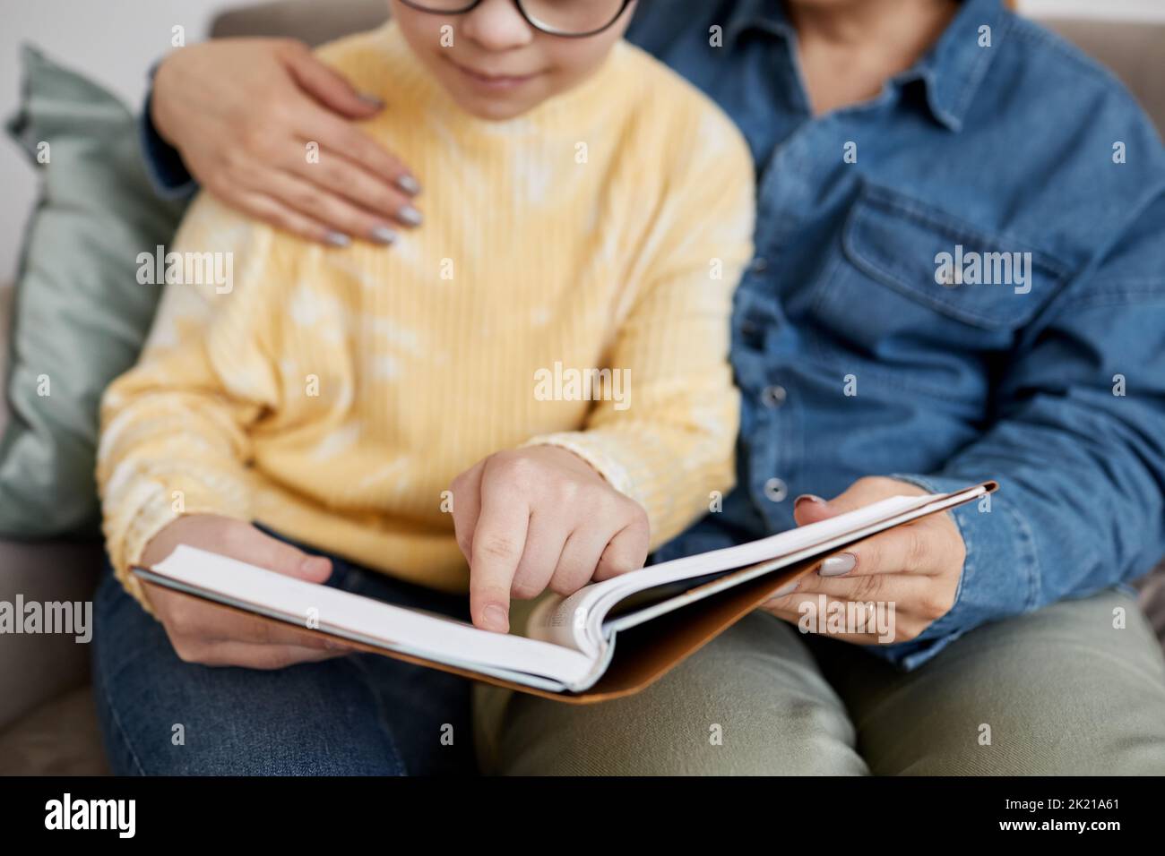 Close up of young girl with Down syndrome reading book with loving mother at home Stock Photo