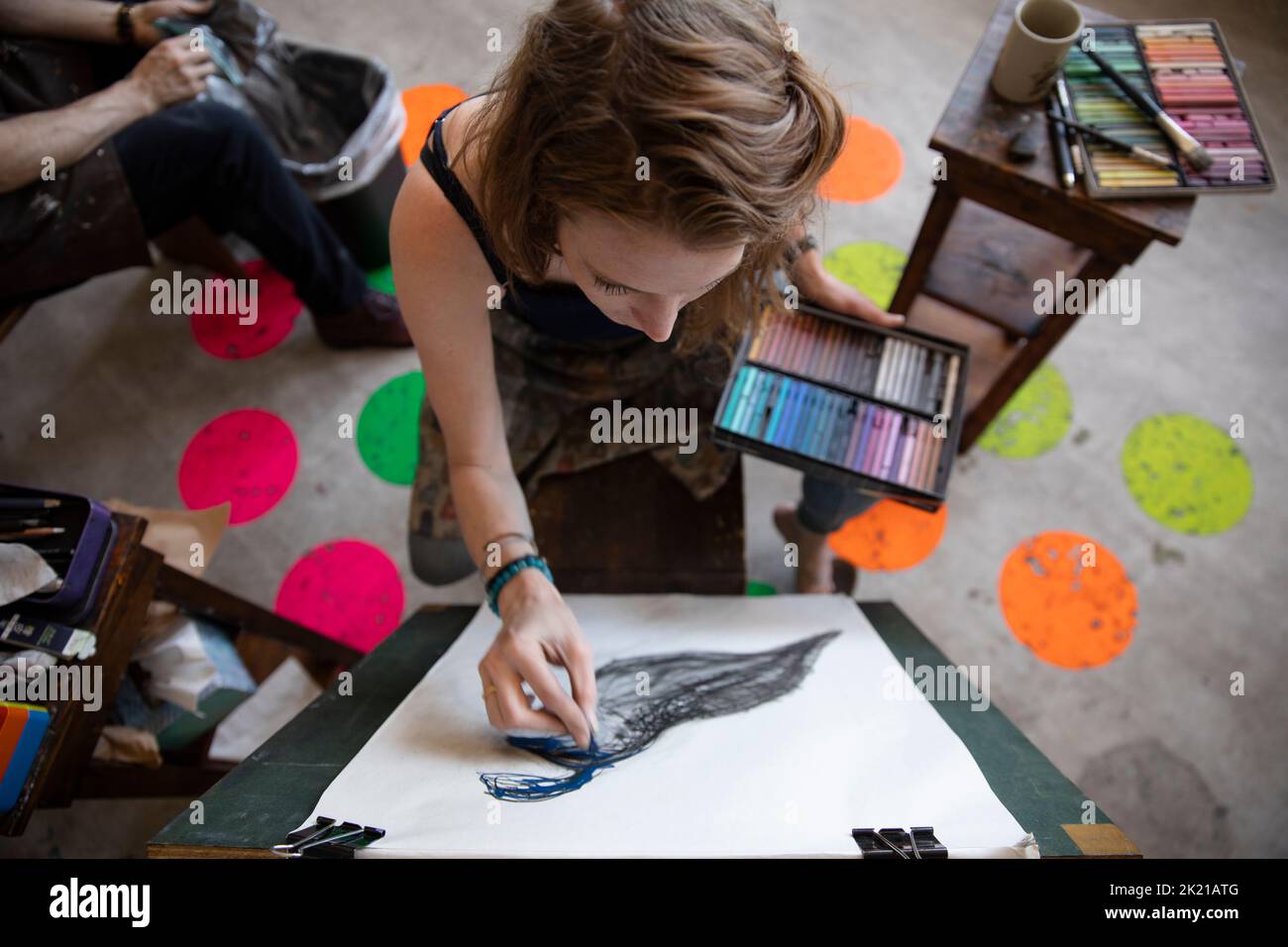 Female artist using chalk on bird drawing at easel in art studio Stock
