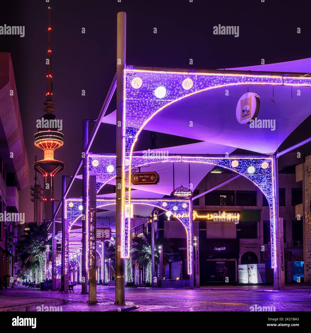 A shot of a purple lighten shopping street with the Liberation Tower in the background at night in Kuwait Stock Photo