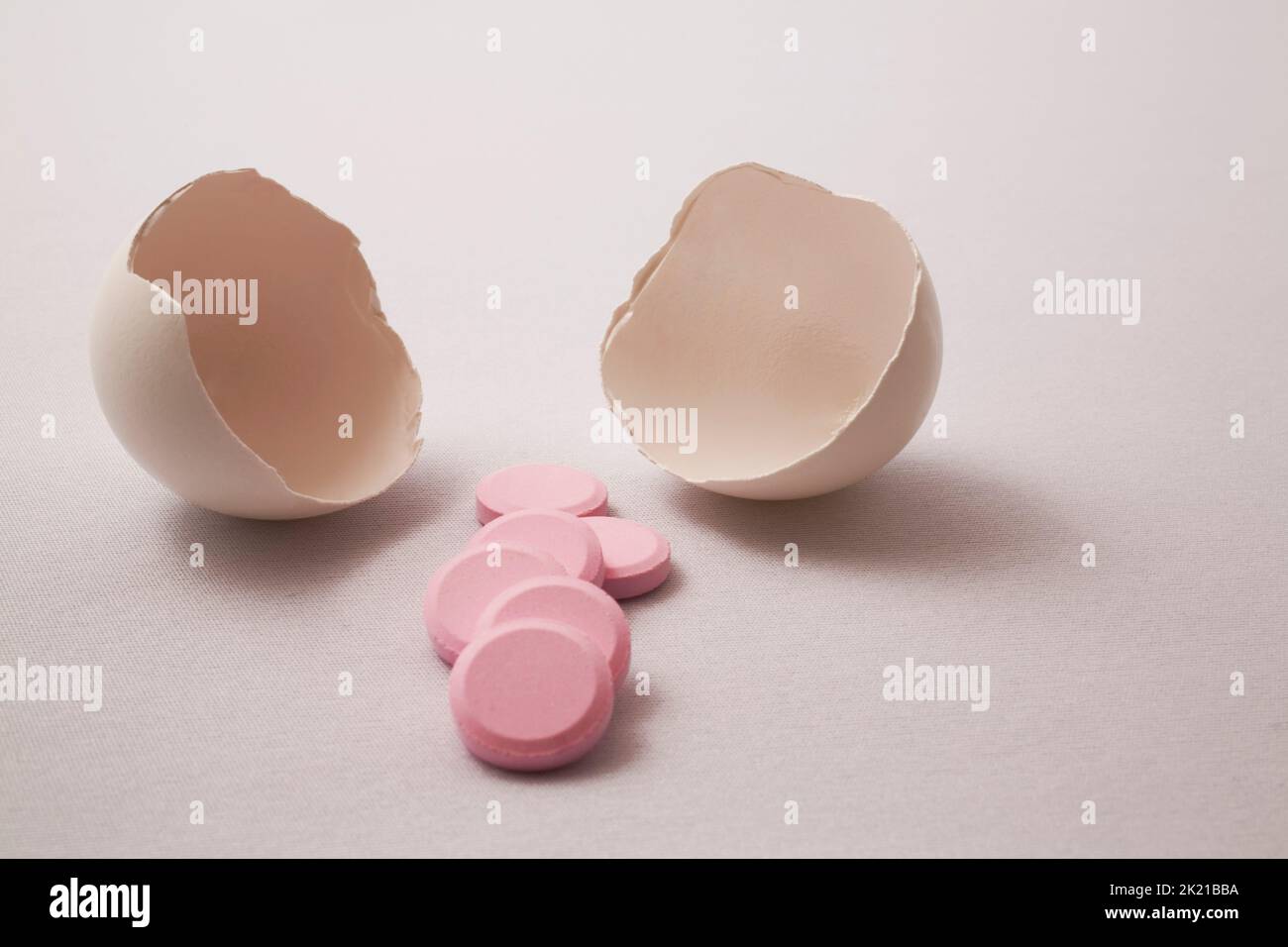 Close-up of cracked egg shells with pink medicine pills on light gray background. Stock Photo