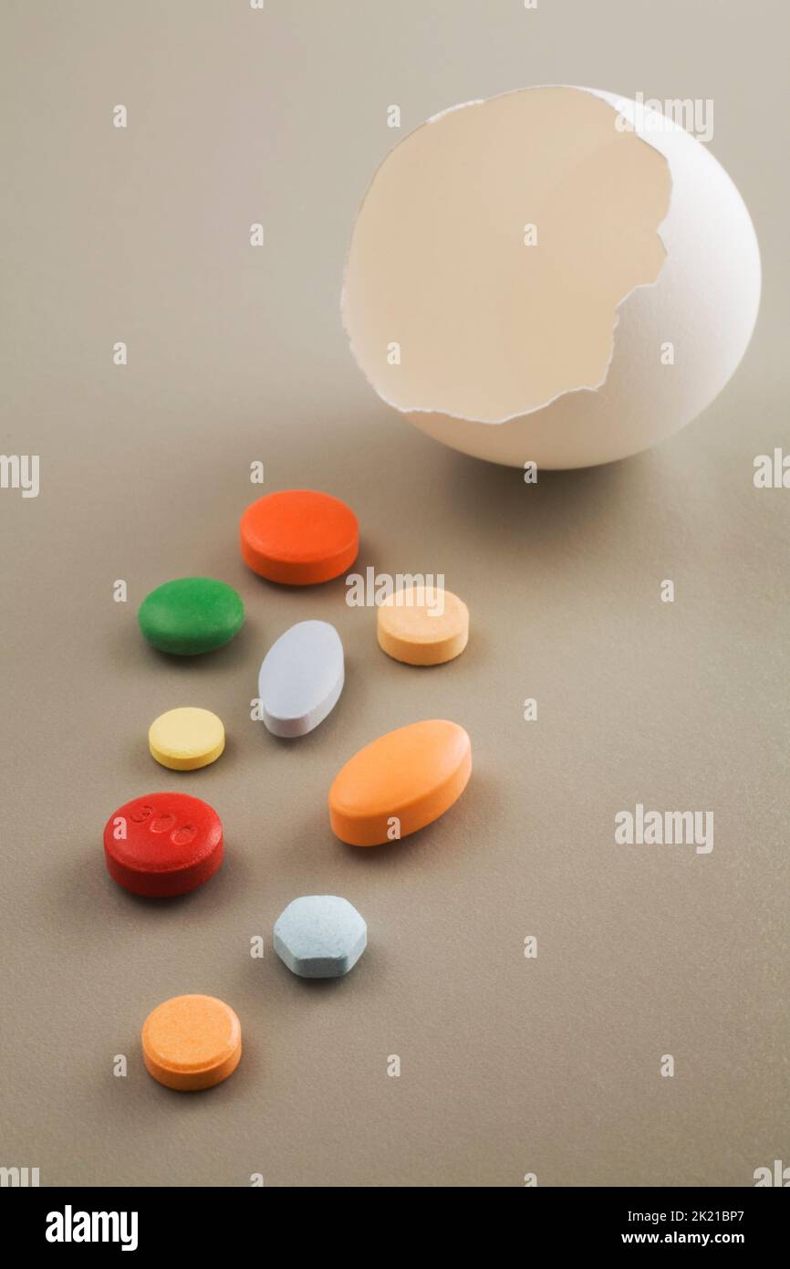 Close-up of cracked egg shell with various colored medicine pills on light gray background, Studio Composition, Quebec, Canada Stock Photo