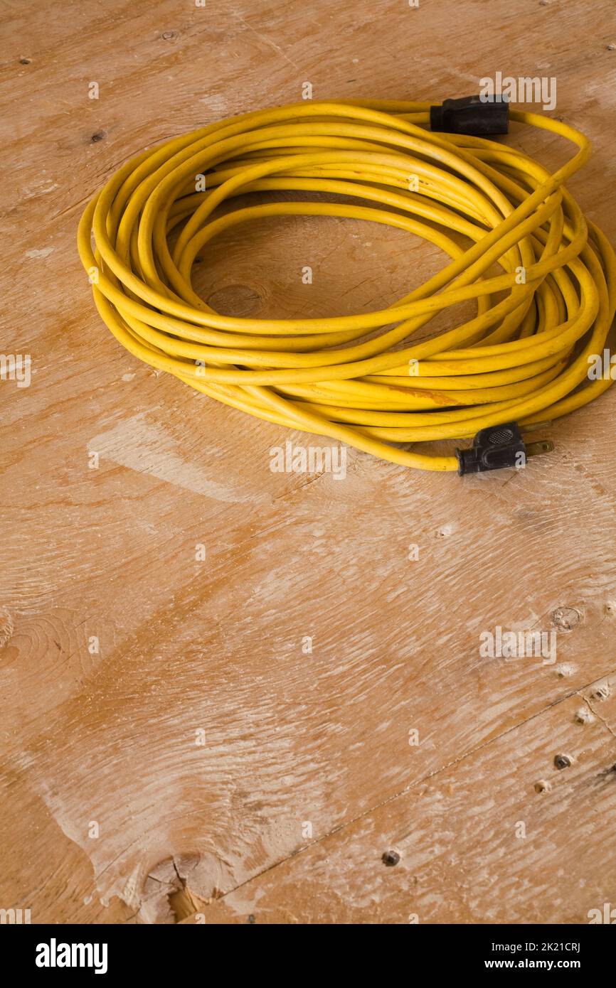 Yellow electrical extension cord on plywood floor inside home. Stock Photo