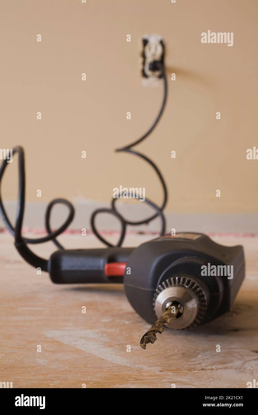 Electric drill on plywood floor plugged into wall outlet inside home, Studio Composition. Stock Photo