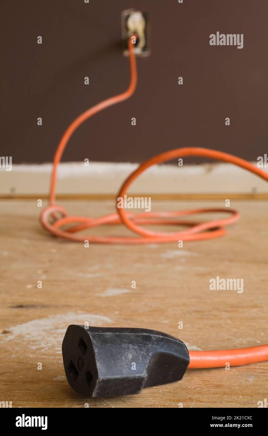Orange electrical extension cord on plywood floor inside home Stock