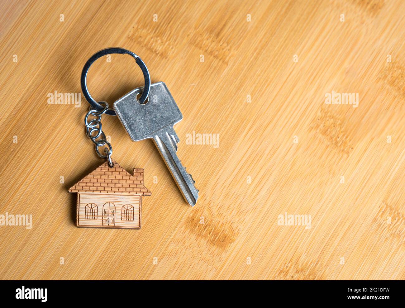 House shaped keychain and key on wood table. Copy space. Stock Photo