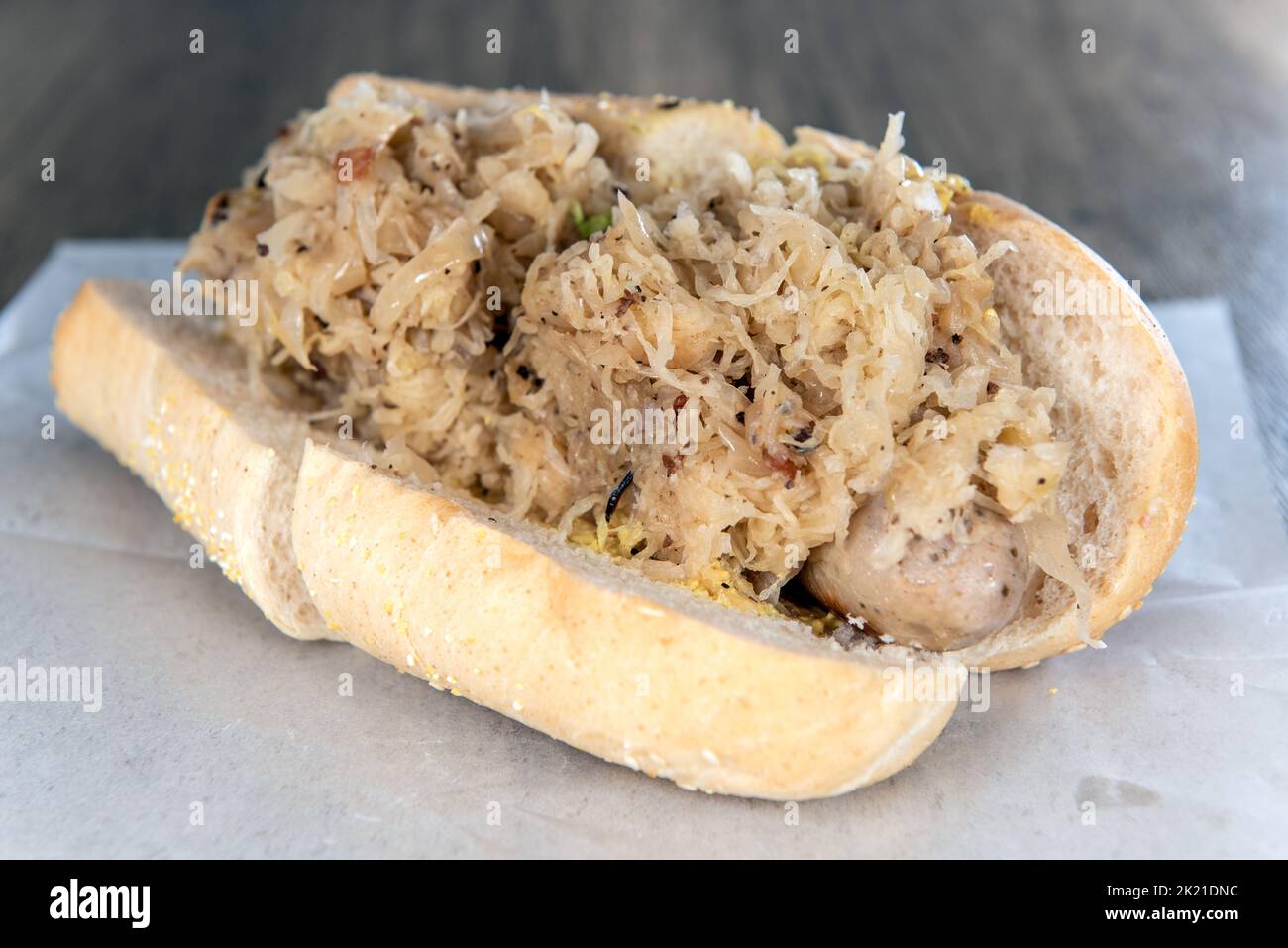Lunch is served with a loaded bratwurst and sauerkraut sandwich overflowing with ingredients. Stock Photo