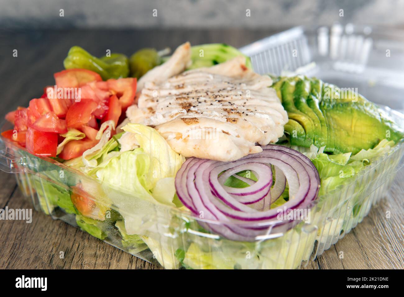 Lunch is served with a loaded grilled chicken breast salad overflowing with ingredients and sliced avocado. Stock Photo