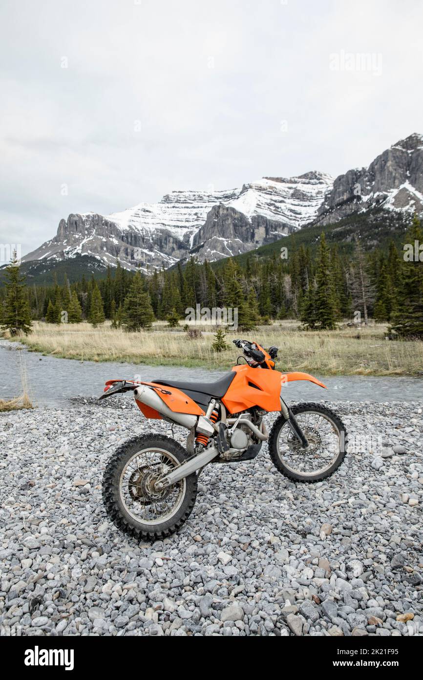 Dirt bike parked at remote stream below Rocky Mountains, Canada Stock Photo