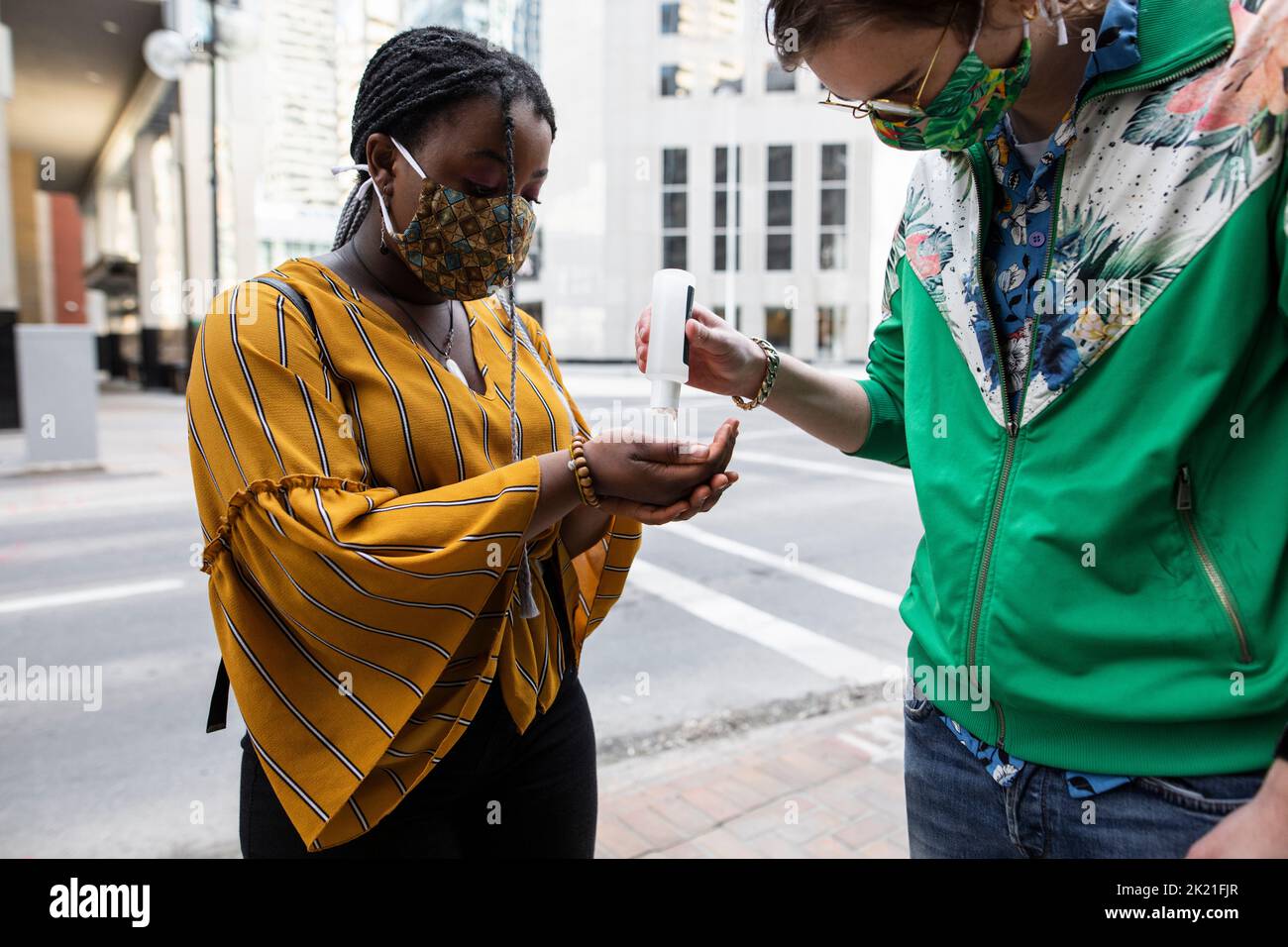 Teenage couple in face masks using hand sanitizer on city street corner Stock Photo