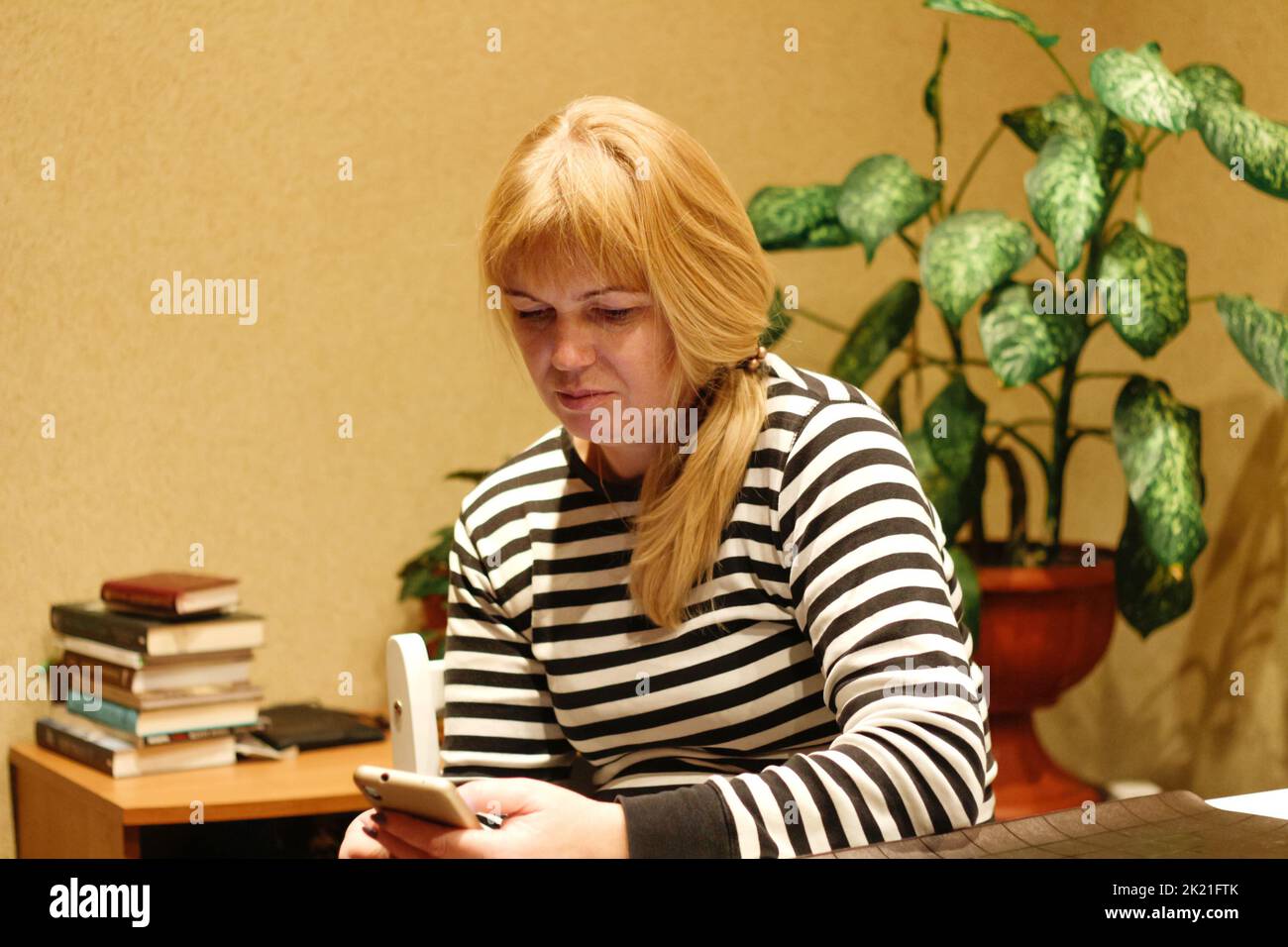 Defocus serious charming woman using smartphone while working at home. Young french blonde woman with ponytail. Reading news. Elegance women scrolling Stock Photo