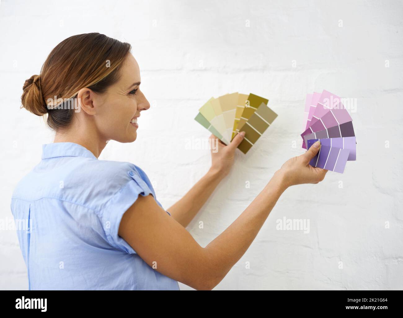 I cant make up my mind. a woman holding up colour swatches uo to the wall. Stock Photo