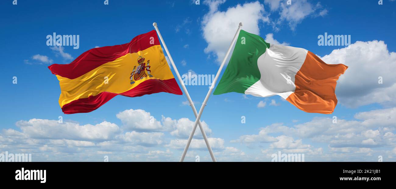 two crossed flags Ireland and spain waving in wind at cloudy sky ...