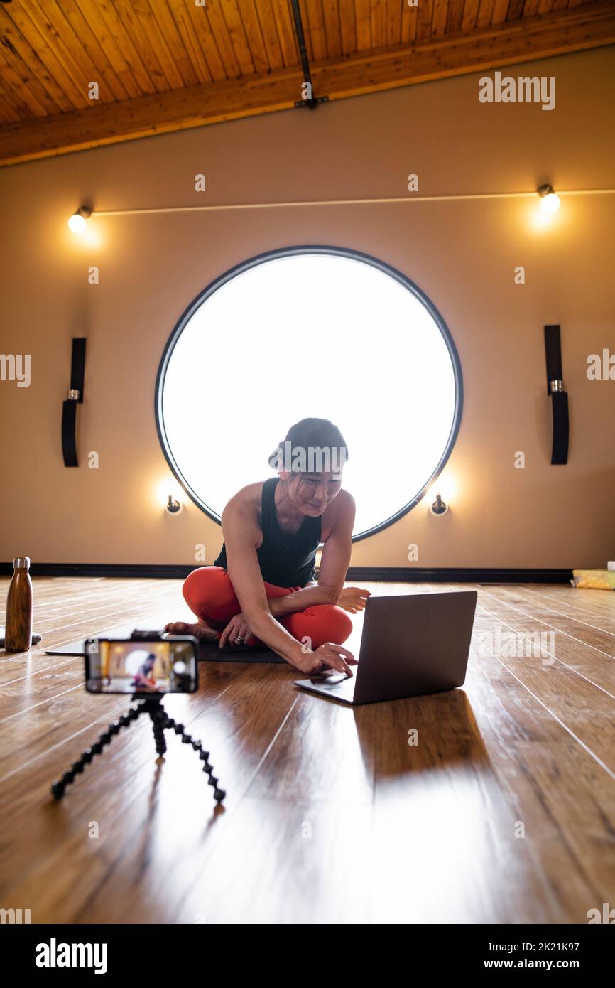 Female yoga instructor at laptop preparing to teach online class Stock