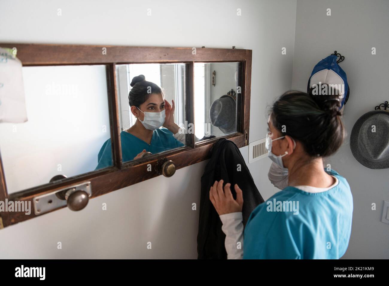 Female nurse in scrubs putting on face mask at mirror Stock Photo - Alamy