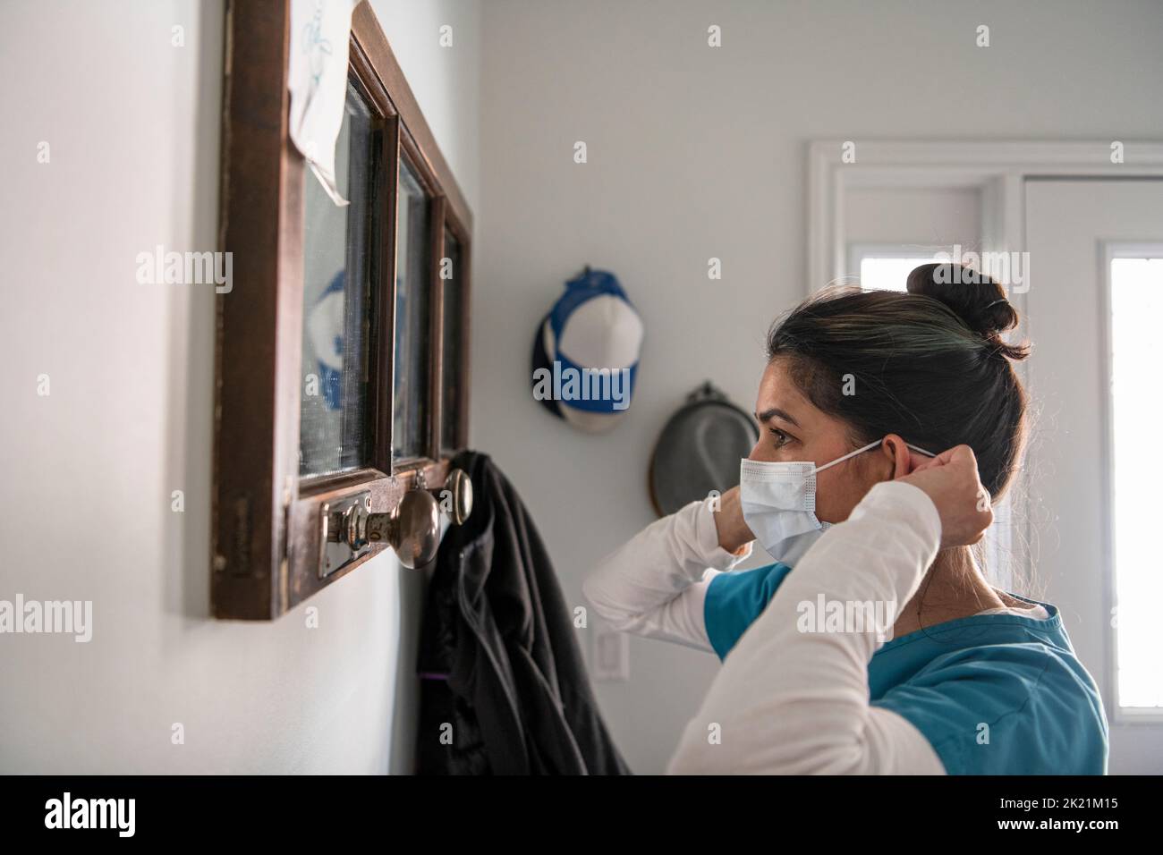 Female nurse putting on face mask at mirror in foyer Stock Photo Alamy