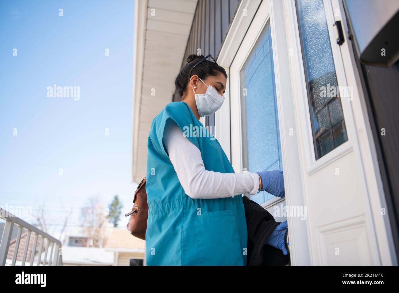 Female nurse in scrubs and face mask locking front door of house Stock Photo