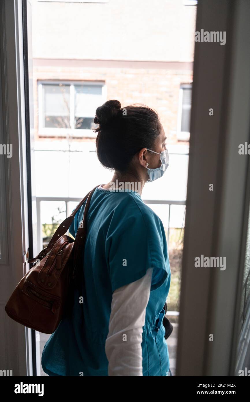 Female nurse in scrubs and face mask leaving front door for work Stock Photo