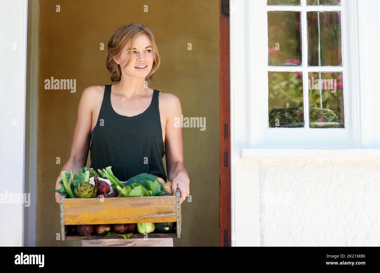 Compliments of the season. A young woman holding a crate of vegetables ...