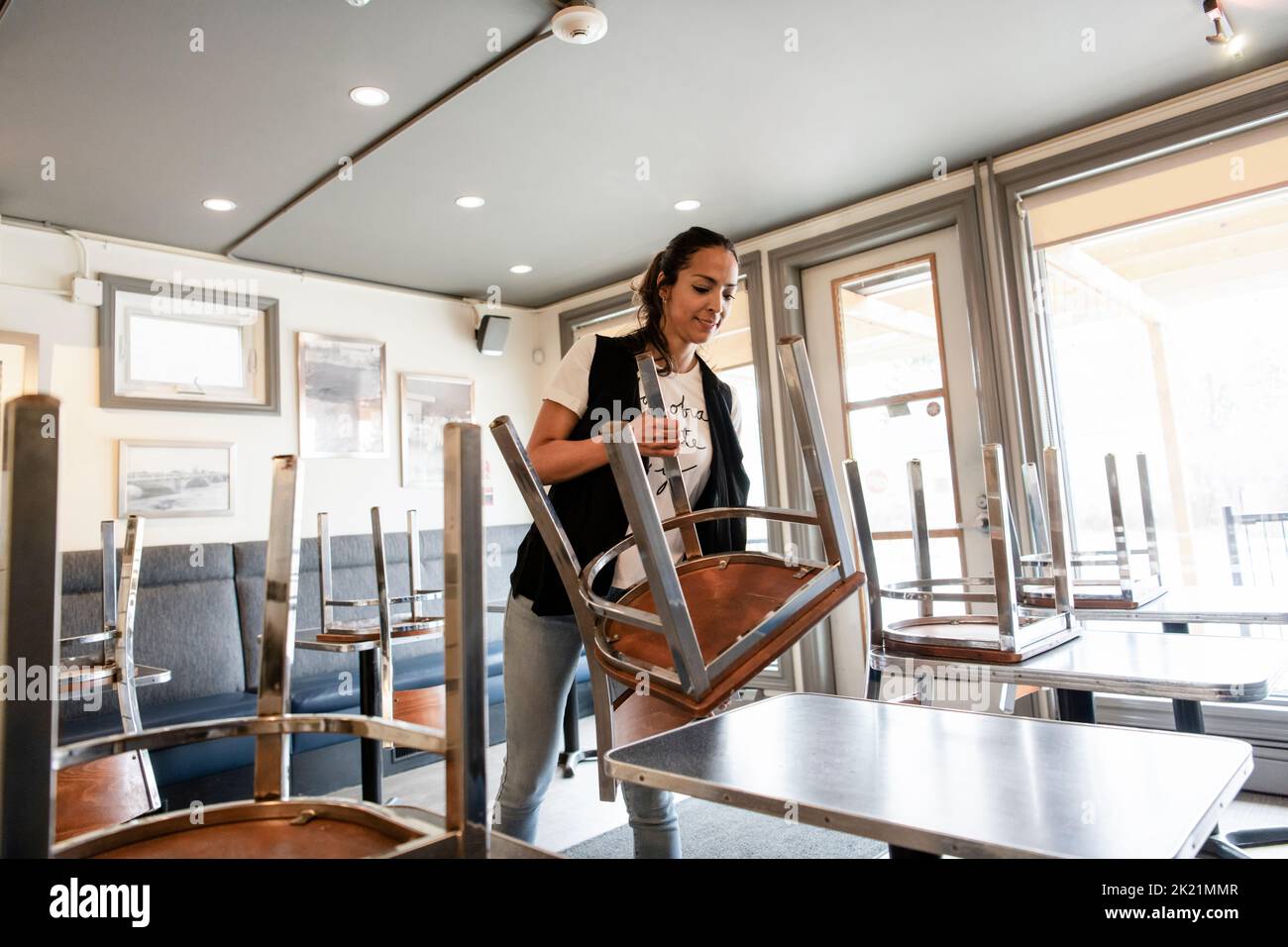 Female business owner removing chairs from table in cafe Stock Photo