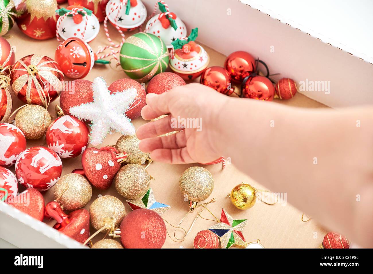 Female hand grabbing ornaments from a box of mixed Christmas tree balls, stars and bells in the classic traditional colors of red, green, white and go Stock Photo