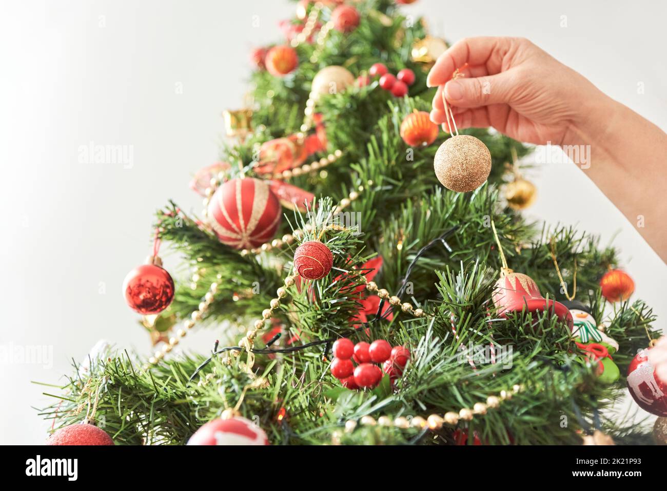 Unrecognizable person decorating a traditional Christmas tree at home, hand hanging golden ball. Subjective point of view, composition with copy space Stock Photo