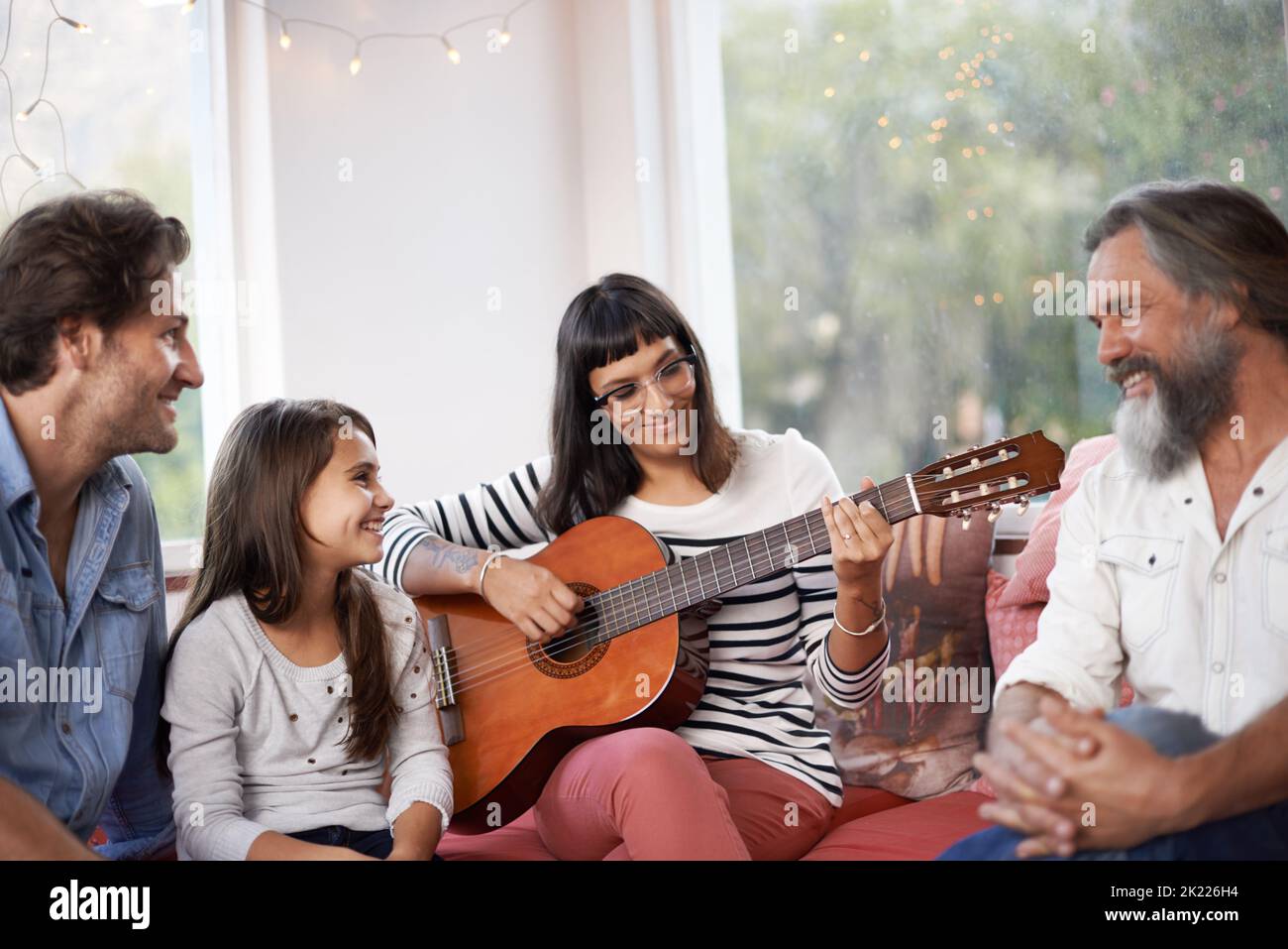 Family fun with the guitar. a woman playing the guitar while sitting with her family. Stock Photo