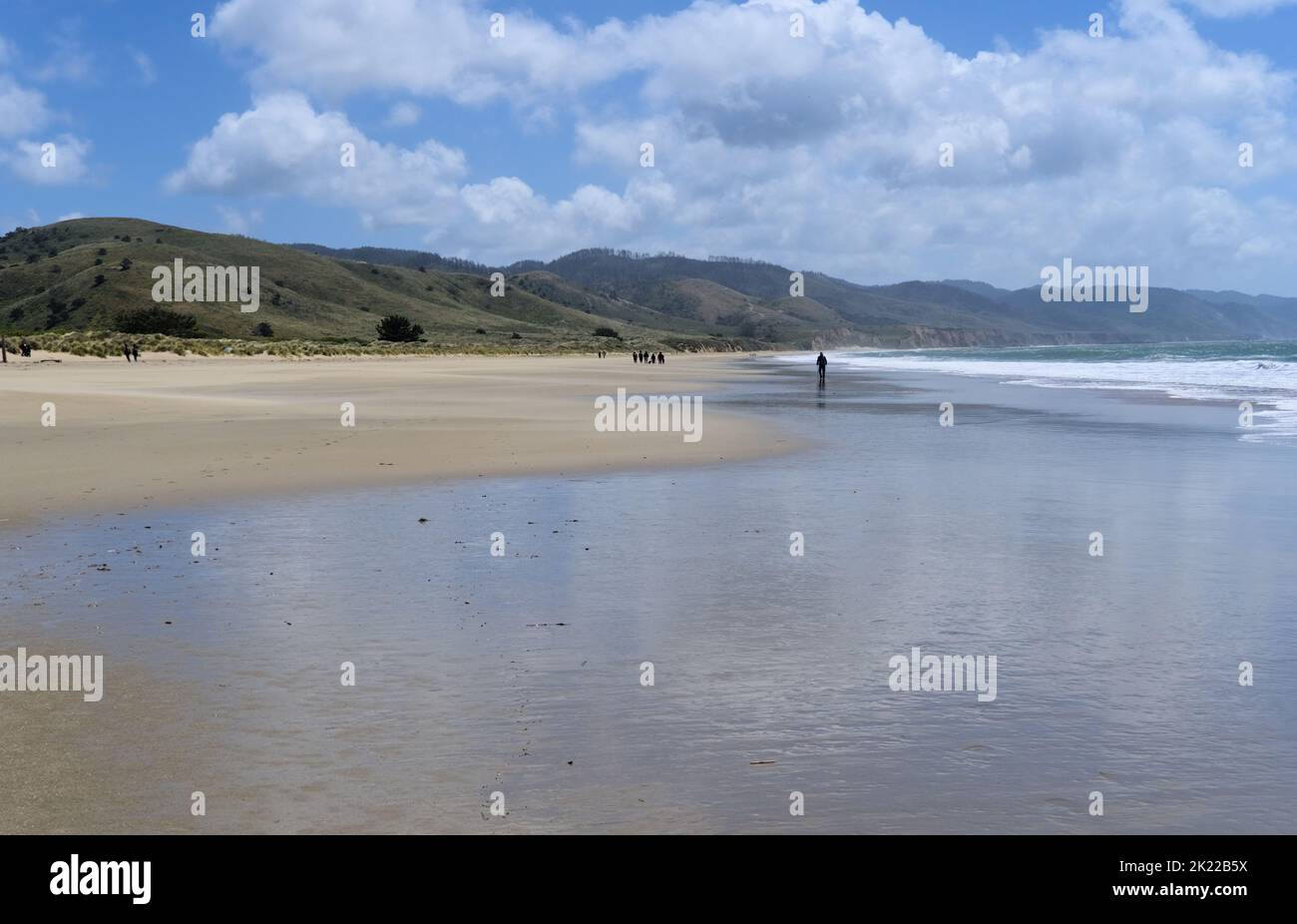 A peaceful beach with the clouds reflection in the water and hills in ...