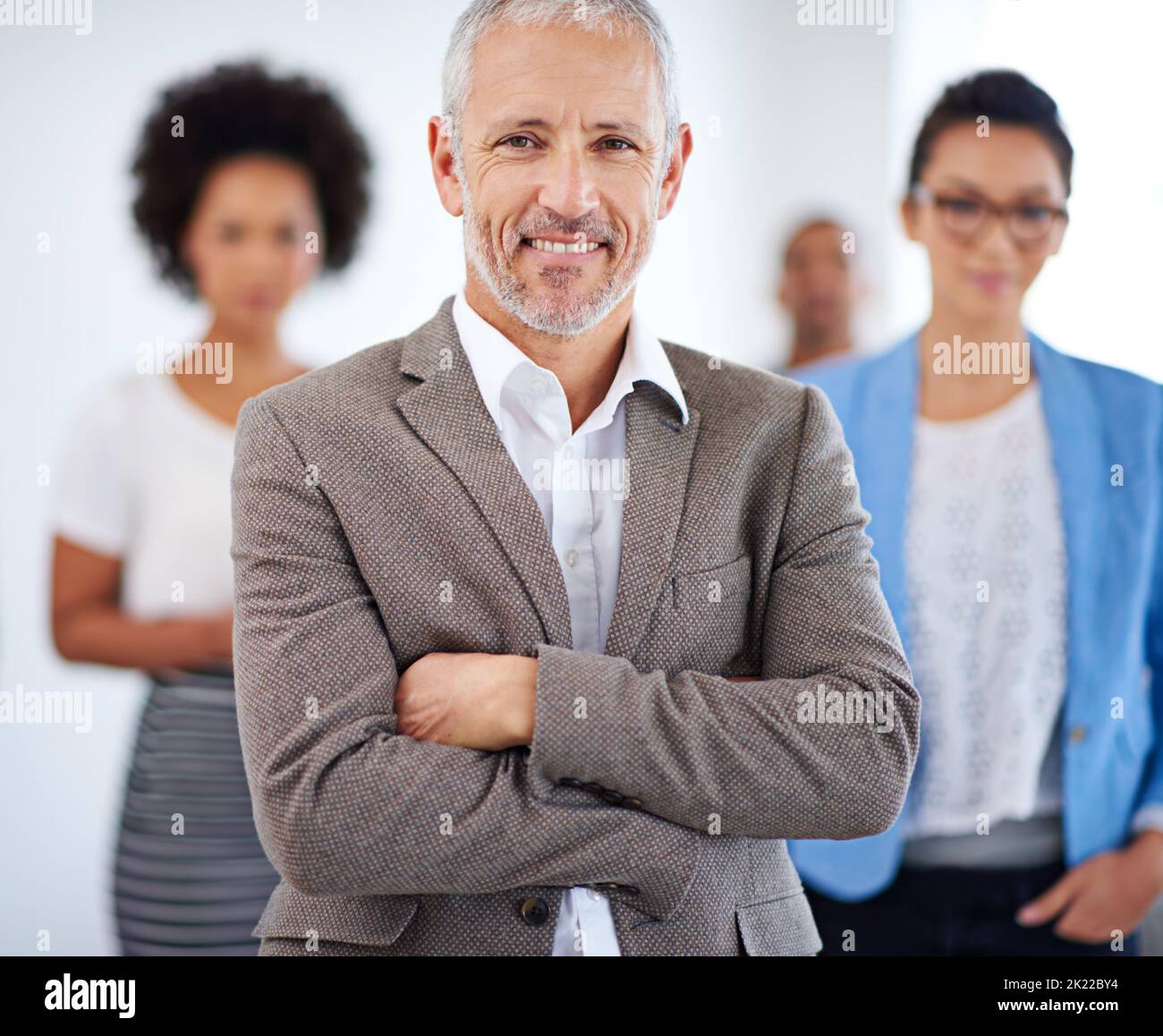 Hes got the maturity to lead well. Mature male office worker standing proudly with coworkers in background. Stock Photo