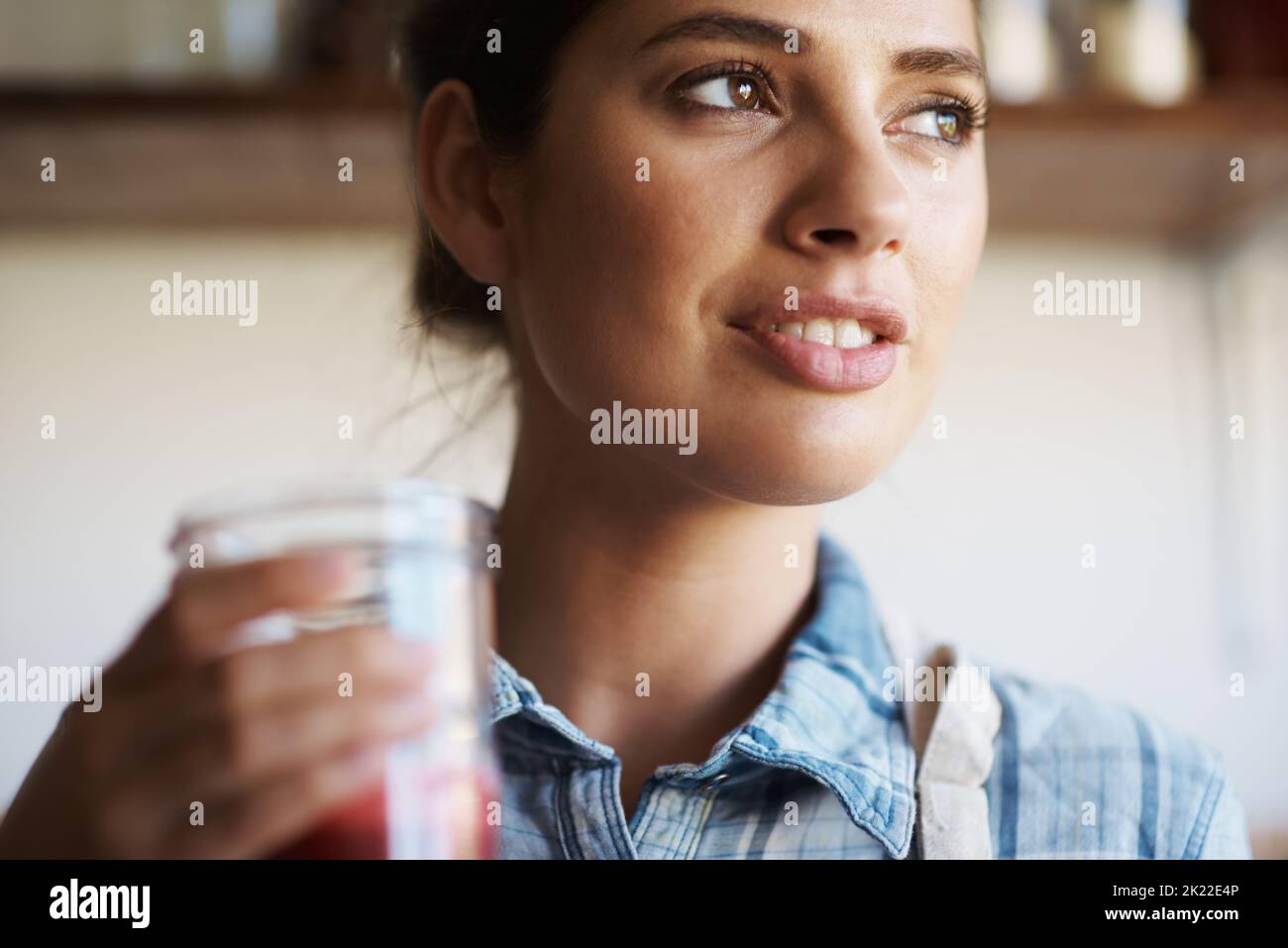 The juice was definitely worth the squeeze. A beautiful young woman standing indoors and drinking freshly-juiced juice. Stock Photo