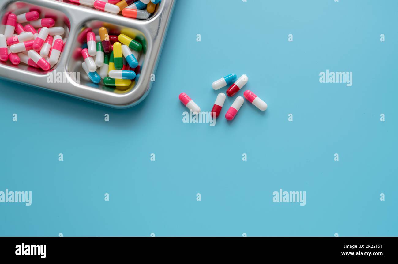 High-angle view of multi-colored antibiotic capsule pills on stainless steel tray and blue background. Antibiotic drug resistance. Prescription drugs. Stock Photo