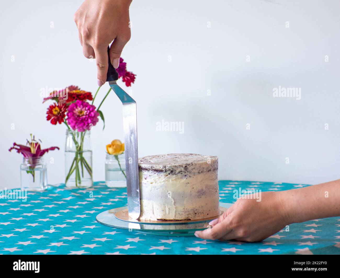 Woman spreading the icing to cover the top of the cake. Home baking, handmade. Free time on quarantine. Female hands level the cream with a spatula an Stock Photo