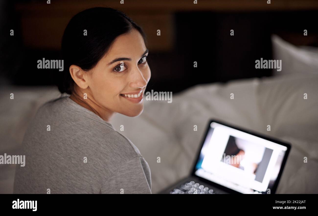Socializing with a friend online. A young woman working on her laptop in bed. Stock Photo