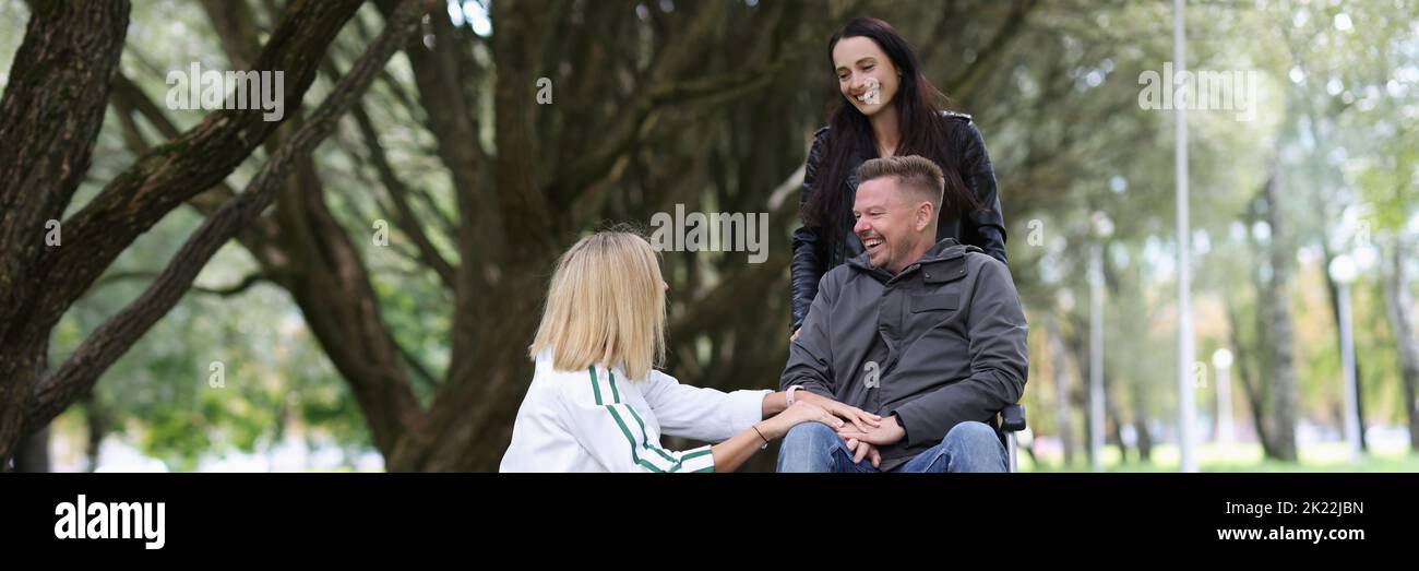 Two women and man in a wheelchair are talking in park Stock Photo - Alamy