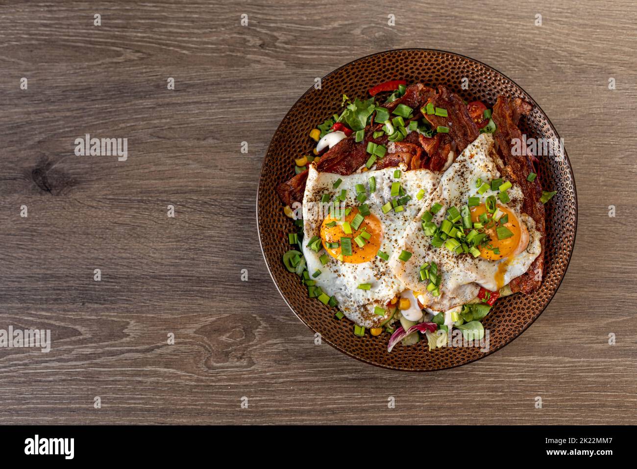Tasty, appetizing fried egg, scrambled egg, with meat and bacon with green grocery and corn on plate on wooden table Stock Photo