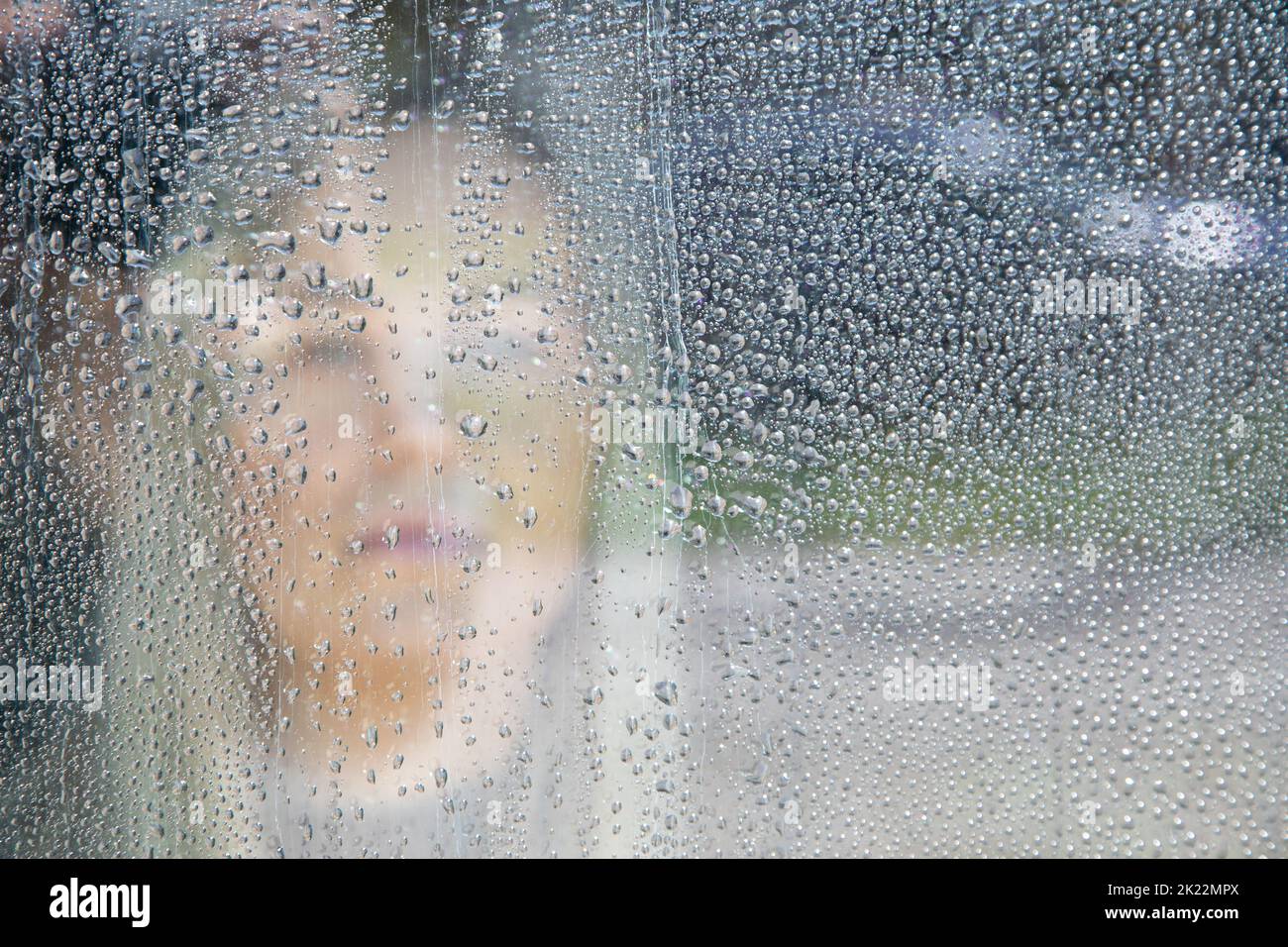 Wet window view of sad, depressed blond woman looking away and thinking of something in rainy weather. Lockdown, sadness Stock Photo