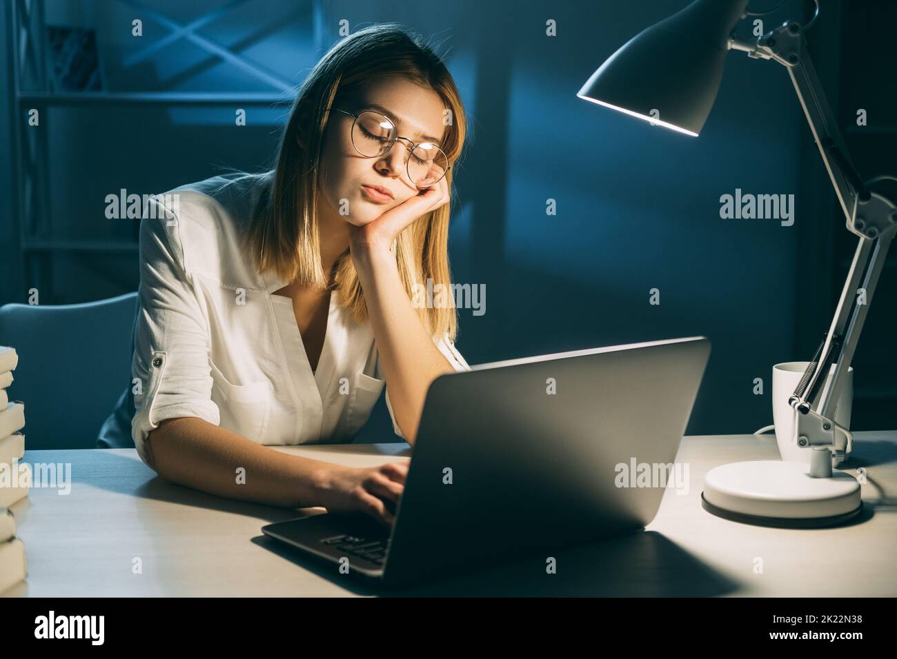 Work fatigue. Overworking from home. Remote job. Sleeping tired exhausted woman working on laptop typing in her dream in dark office workspace Stock Photo