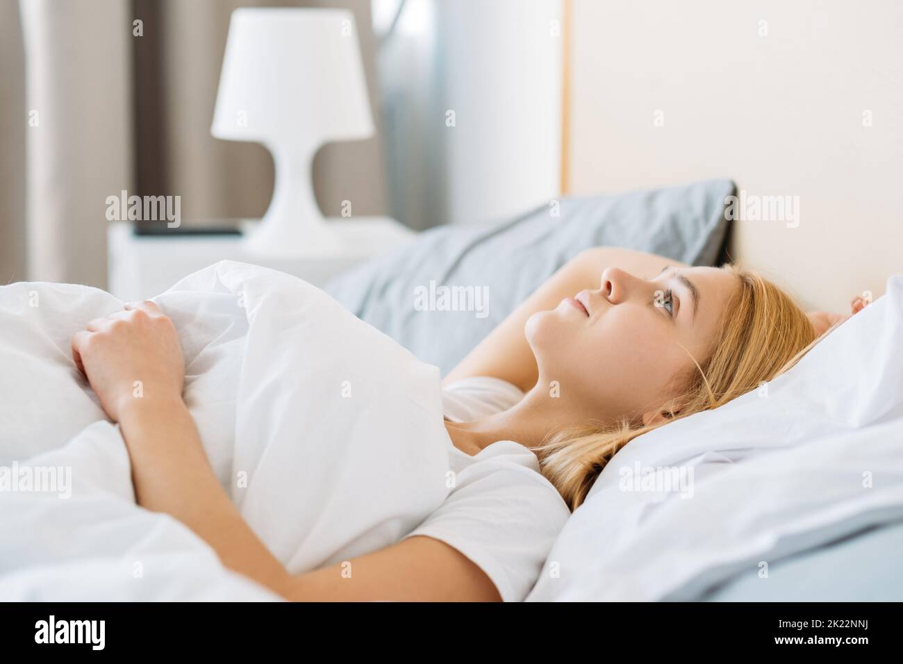 Bedroom relax. Healthy rest. New day. Slept well. Peaceful dreamy fresh awake young woman under blanket in soft clean white cozy bed sheet enjoying go Stock Photo