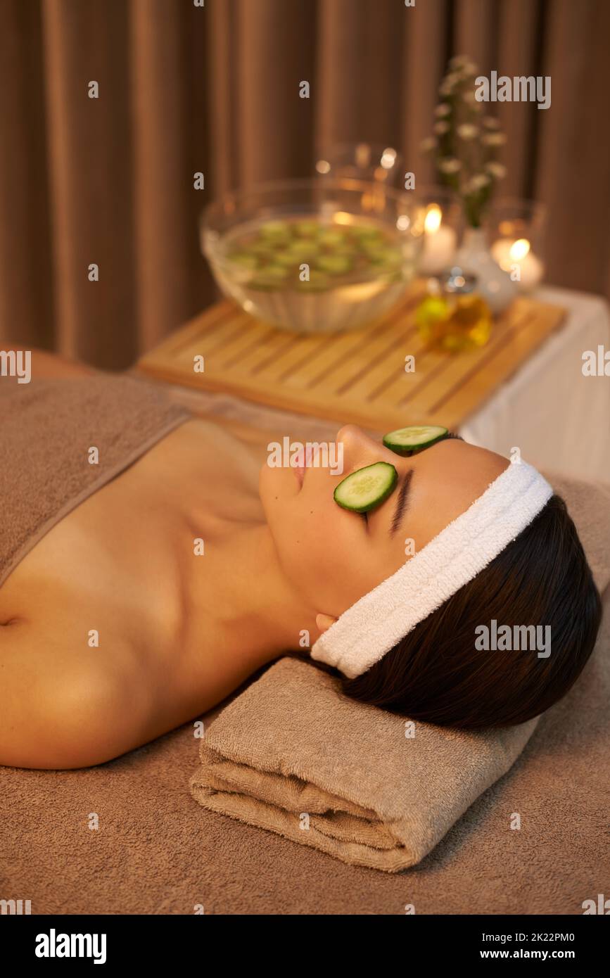 Letting the cucumbers work their magic. A beautiful young woman lying on a massage table at the spa with cucumer over her eyes. Stock Photo