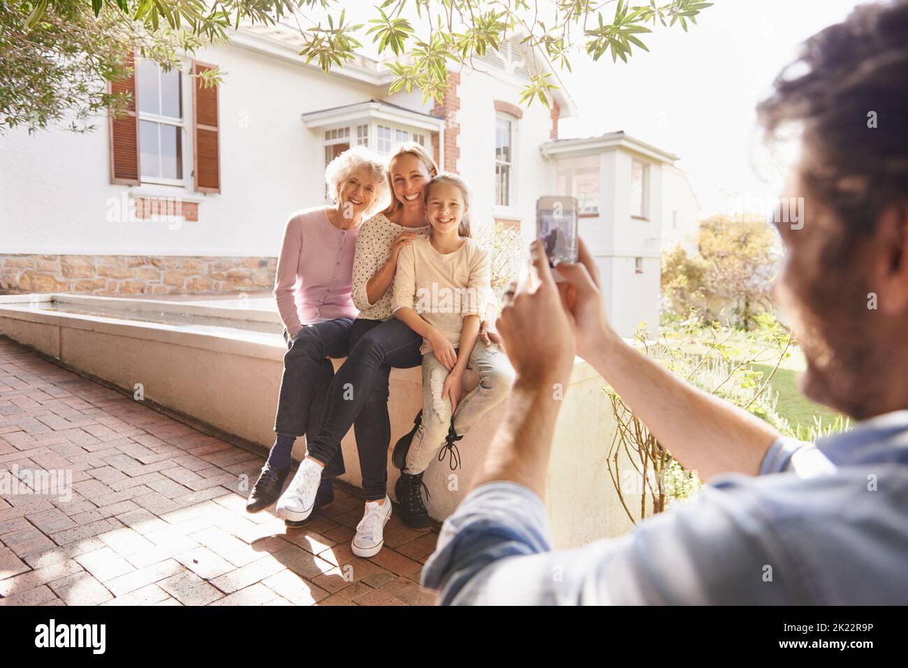 Capturing beautiful family moments. A man using his smartphone to take a photo of his family sitting outdoors. Stock Photo
