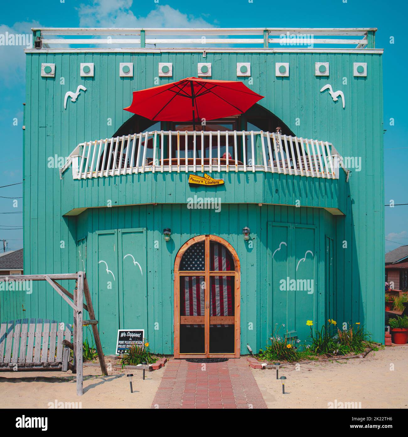 A beautiful teal boardwalk house with a walkway and a red umbrella on